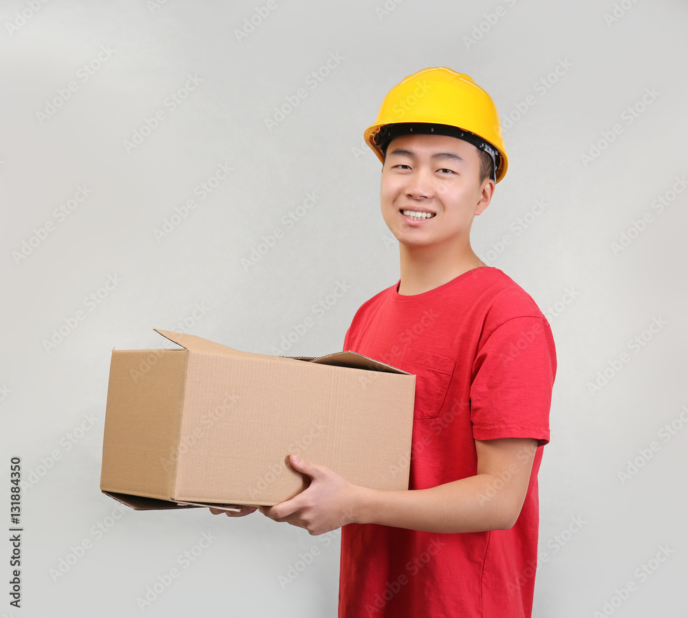 Asian warehouse worker with cardboard box on light background Asian warehouse worker with cardboard box on light background
