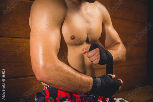 Athlete wrapping his hands before the fight while sitting on a bench isolated with brown wooden background