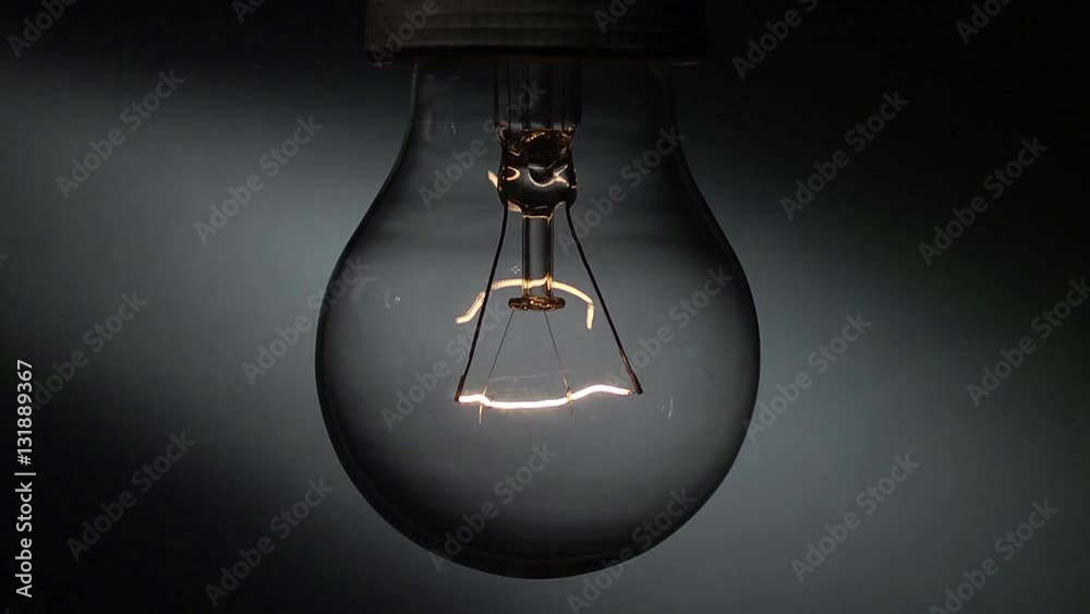 Una vecchia lampada al tungsteno in primo piano si accende e si spegne lentamente.