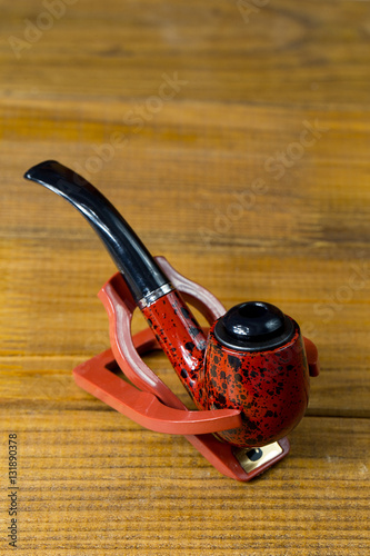 red-black classic tobacco pipe on a stand, brown wooden backgro