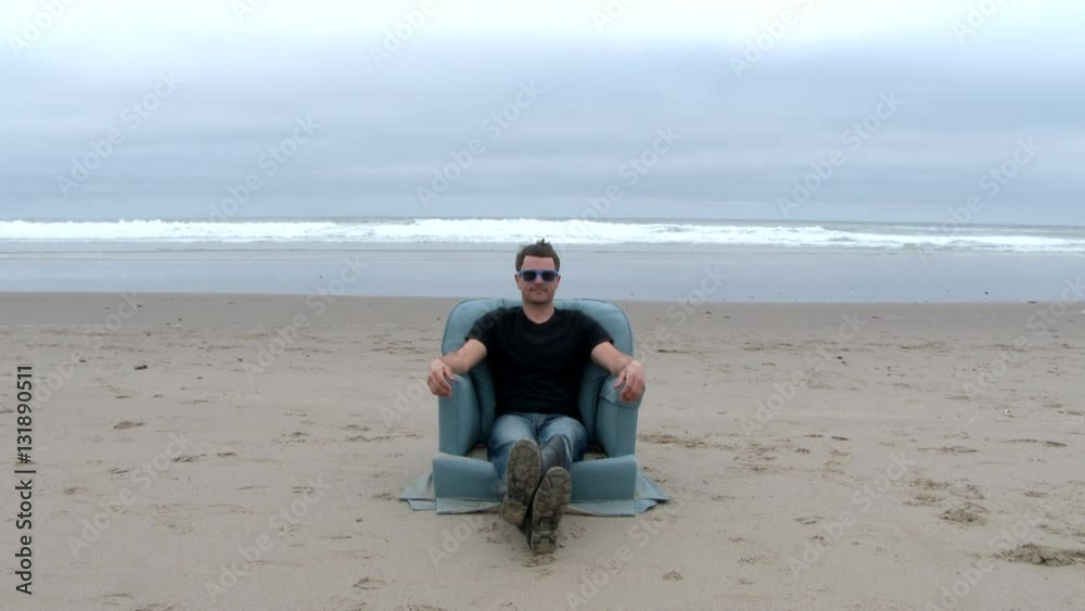 Man sitting on cozy armchair lifts hand and clicks an invisable remote control at the Oregon Coast. Man sitting on cozy armchair lifts hand and clicks an invisable remote control at the Oregon Coast.