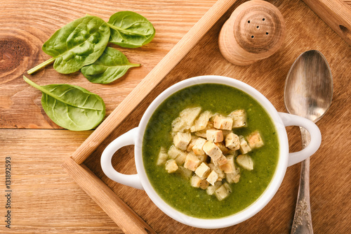 Green cream vegetable soup with croutons on wooden tray.