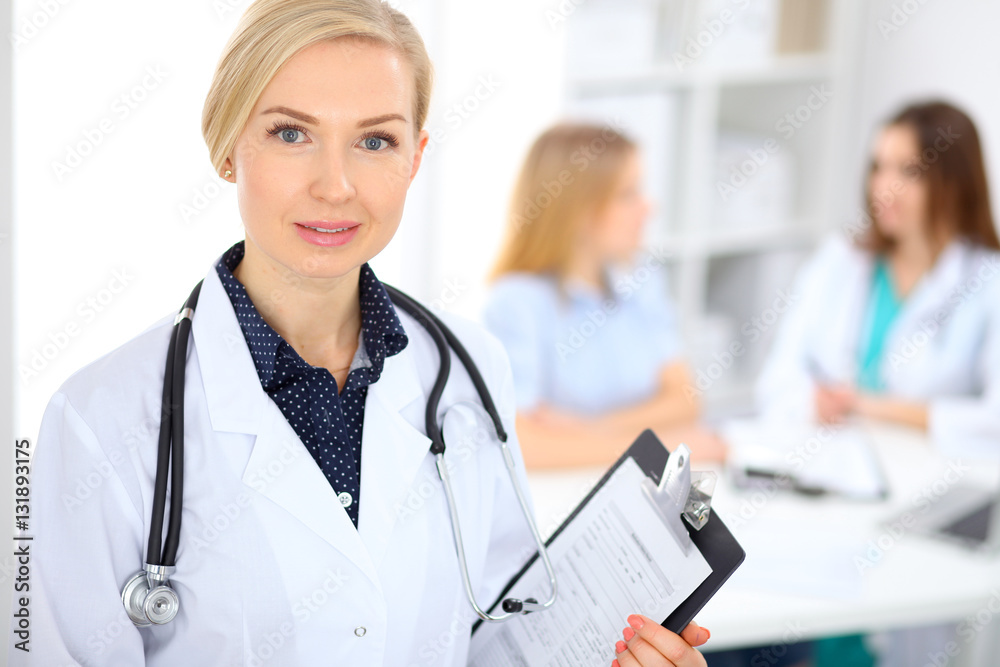 Female doctor smiling on the background with patient and his physician in hospital Female doctor smiling on the background with patient and his physician in hospital