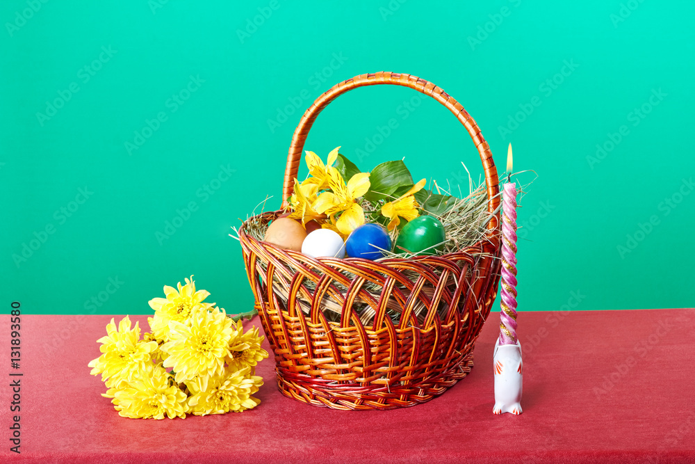 Easter basket with flowers and Easter eggs near a burning candle Easter basket with flowers and Easter eggs near a burning candle