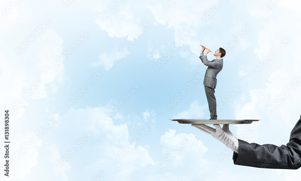 Businessman on metal tray playing fife against blue sky background Businessman on metal tray playing fife against blue sky background
