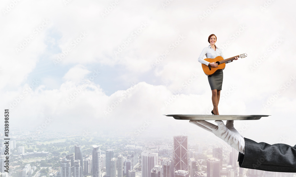 Attractive businesswoman on metal tray playing acoustic guitar against cityscape background