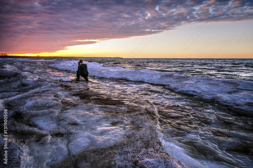 Male Photographer On Frozen Lake. Young professional male photographer kneeling on a frozen lake. Port Austin, Michigan.