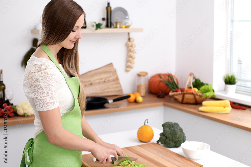 Young woman in the green apron cooking in the kitchen. Housewife slicing fresh salad Young woman in the green apron cooking in the kitchen. Housewife slicing fresh salad