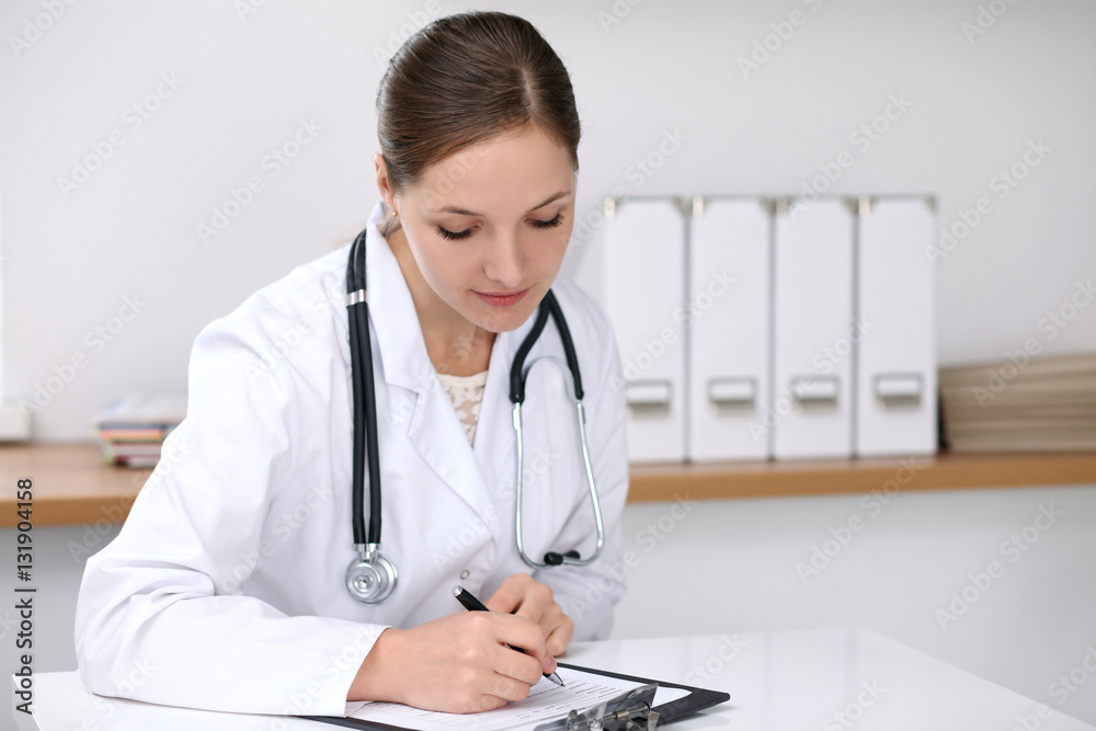 Doctor woman filling up medical form while sitting at the desk. Medicine and health care concept Doctor woman filling up medical form while sitting at the desk. Medicine and health care concept