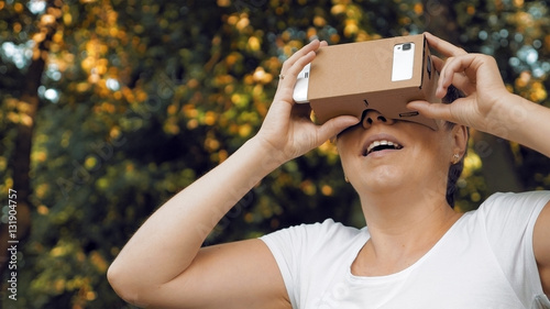 Woman explores virtual reality using cardboard VR glasses. Augmented reality quickly comes in human lives. VR mounted displays helmets and glasses are the most popular devices for playing AR games.