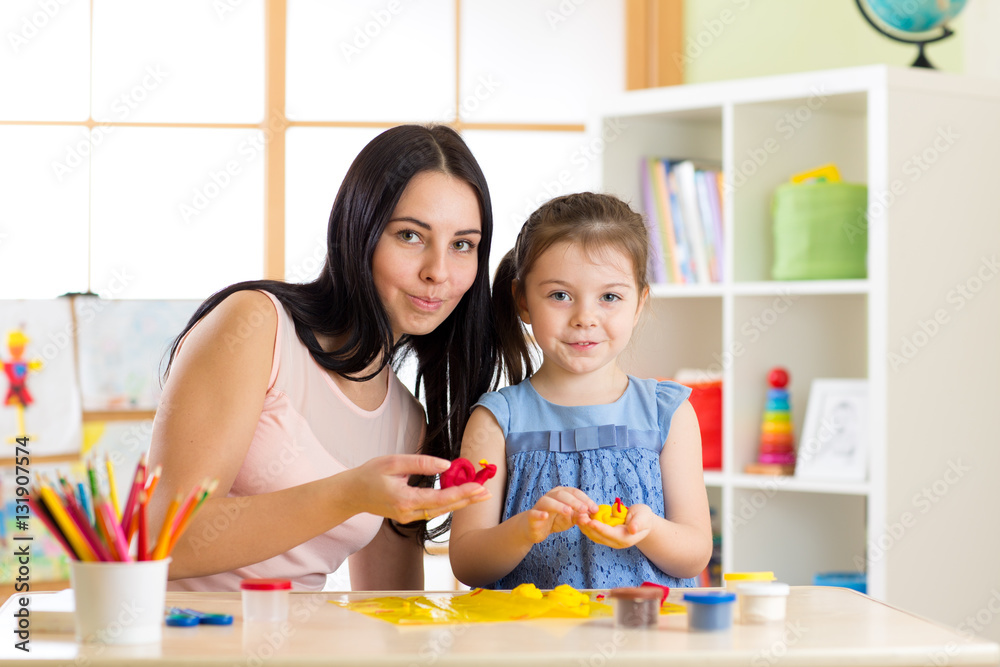 Fototapeta premium Teacher and little girl kid learn mold from plasticine in kindergarten