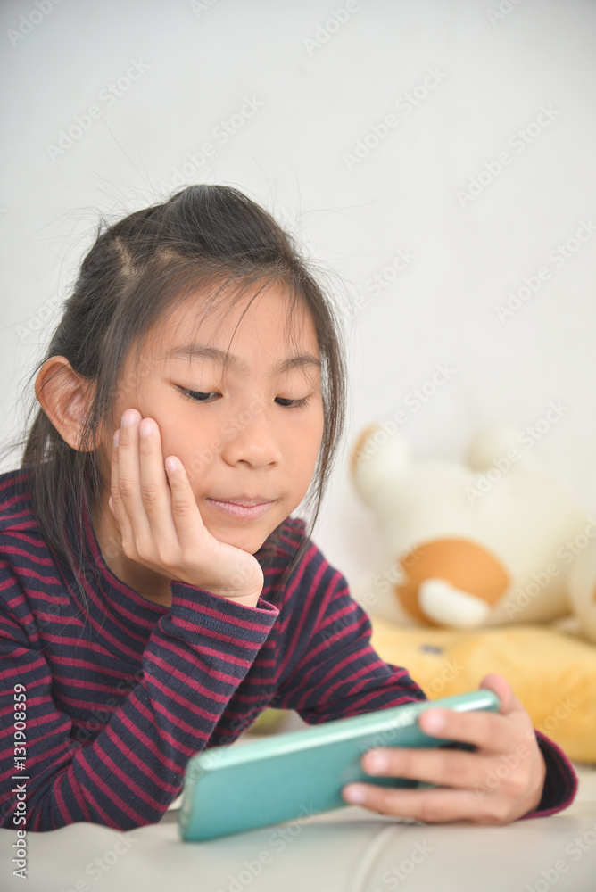 Happy Asian child girl looking at smart phone on bed at home. Happy Asian child girl looking at smart phone on bed at home.