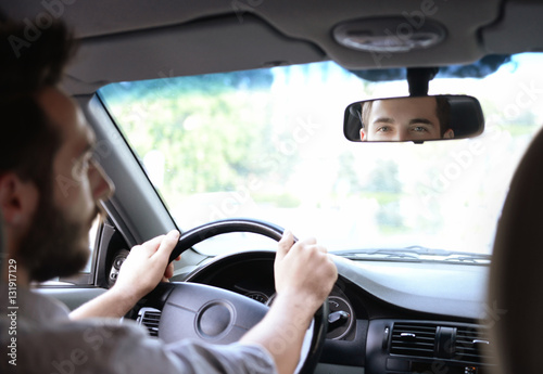 Young successful driver looking in rear view mirror