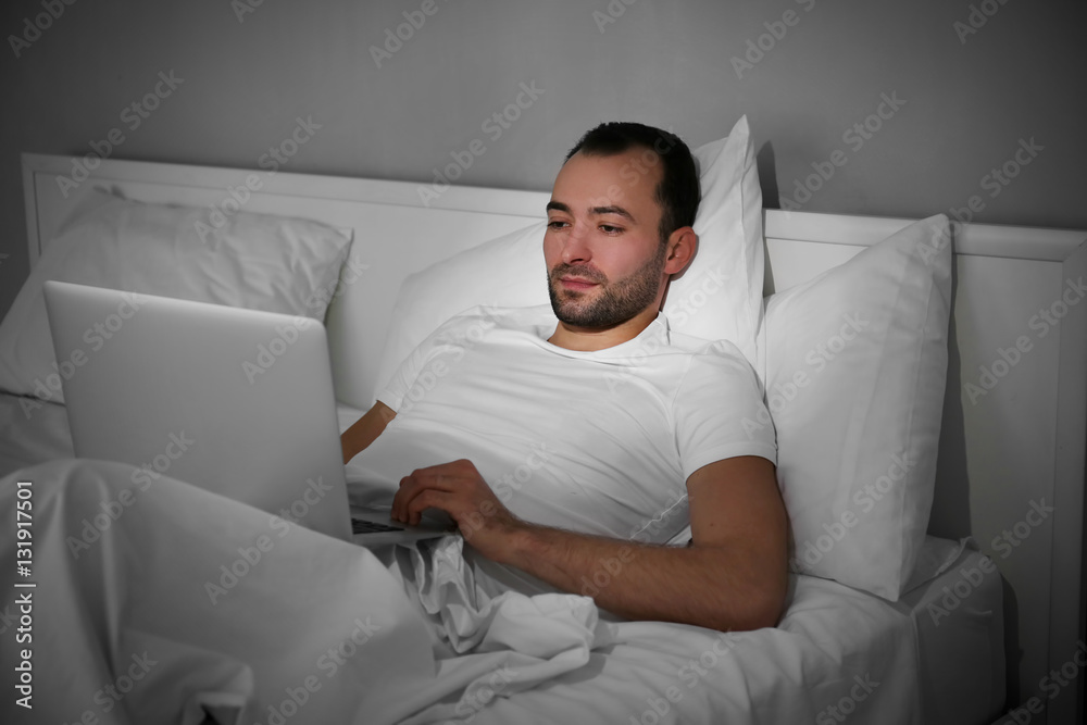 Fototapeta premium Young man with laptop lying in bed