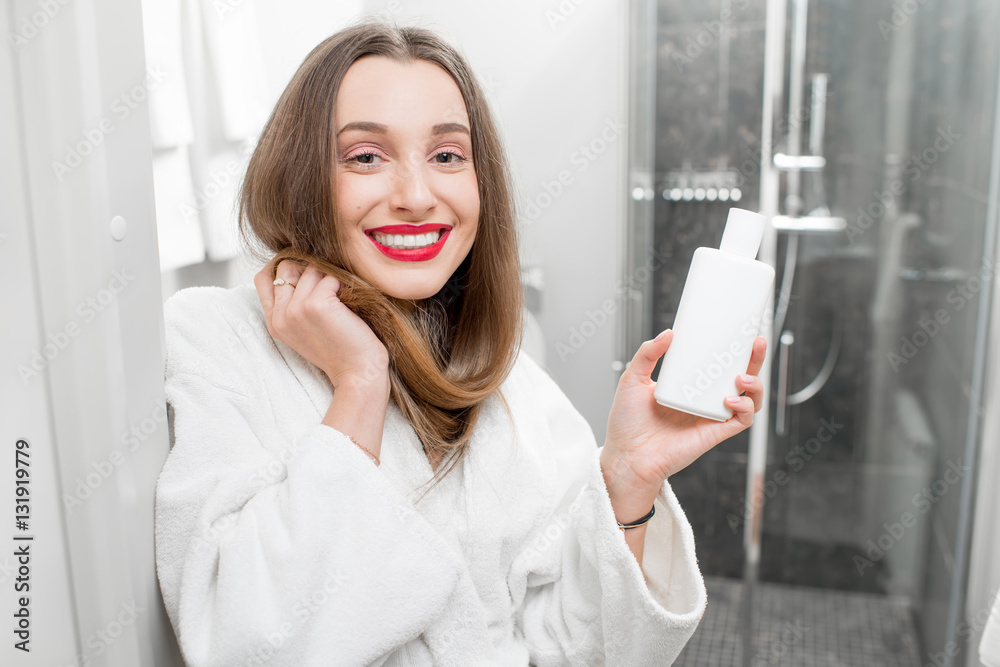 Happy woman with healthy hair holding a bottle with shampoo or conditioner in the bathroom Happy woman with healthy hair holding a bottle with shampoo or conditioner in the bathroom