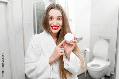 Happy woman holding bottle with cream in the bathroom