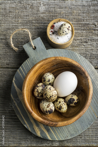 Quail eggs in a wooden bowl on cutting board dark background with salt. Top view