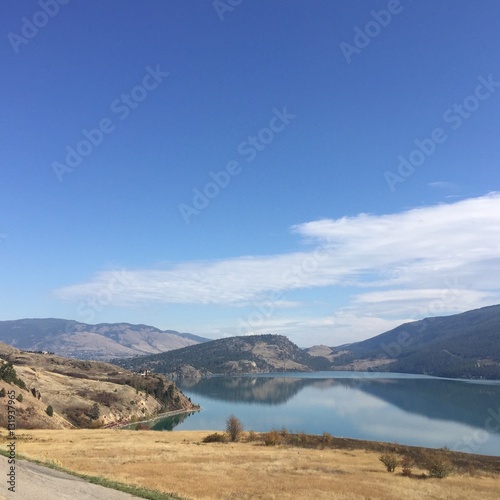 Calm lake, mountains and blue sky landscape in summer. Scenic landscape view with blue sky and white clouds over lake with hills background and water reflections. 