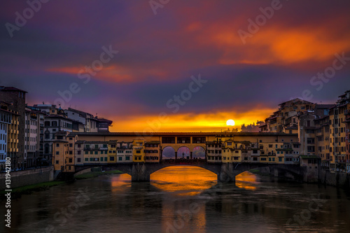 Rising sun peeking out through breaking storm clouds over the Ponte Vecchio in Florence  Italy