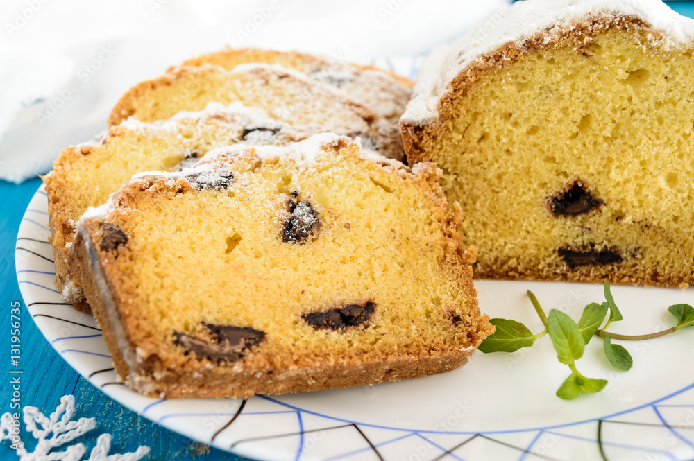 Freshly baked homemade cakes, decorating the top with powdered sugar, cut slices, with pieces of chocolate on a plate on blue background. Close up Freshly baked homemade cakes, decorating the top with powdered sugar, cut slices, with pieces of chocolate on a plate on blue background. Close up