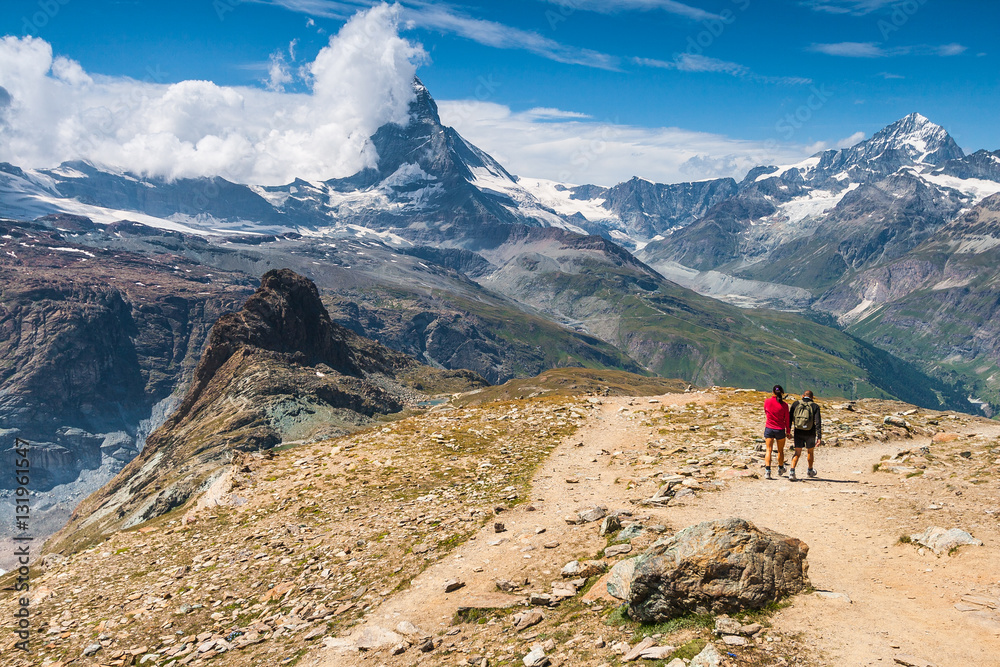 Hikers walking on spectacular mountain scenery, Matterhorn in background, Alps, Switzerland.