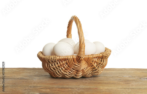 Raw eggs in wicker basket on wooden table