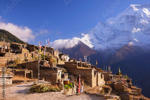 Traditional nepalese village on Pisang region with buddhist praying flags and North Face of Annapurna II mountain summit on background, Annapurna Circuit Trek, Himalaya, Nepal, Asia. horizontal view photo