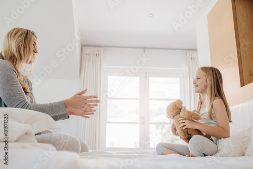 Little girl and woman playing with teddy bear.