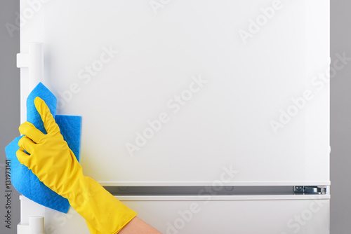 Hand in yellow glove cleaning white refrigerator with blue rag