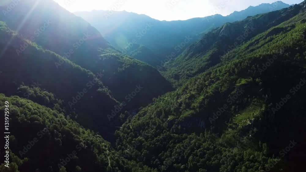 ripresa aerea panoramica tra nella valle delle montagne sopra al torrente con acqua che scorre sulle rocce, in una soleggiata giornata di estate