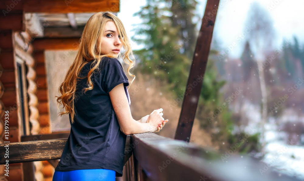 beautiful girl standing on the porch of a wooden house in the winter forest and languid tenderly looks