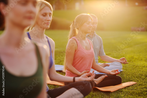 young people in colored clothes doing yoga on fresh grass photo