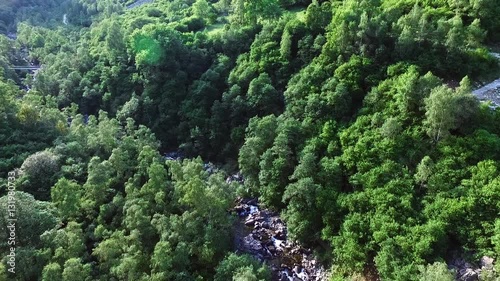 ripresa aerea panoramica tra gole delle montagne sopra al torrente con acqua che scorre sullo sfondo, in una soleggiata giornata di estate