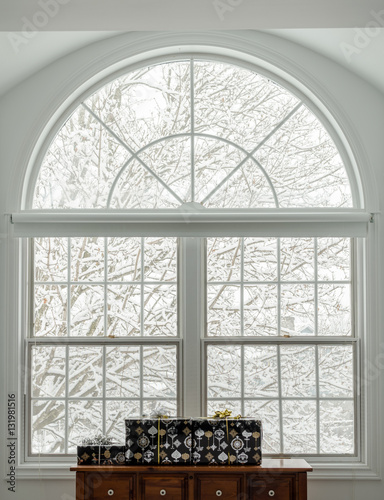 Presents under a white transom window with a snowy scene outside