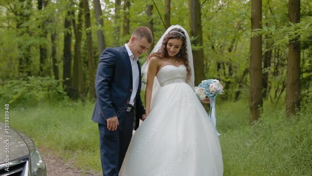 Bride and groom pose in the wood. Young man and woman gently look at each other standing near the wedding decorated car.Beautiful background. Happy moment of loving couple. Bride and groom pose in the wood. Young man and woman gently look at each other standing near the wedding decorated car.Beautiful background. Happy moment of loving couple.