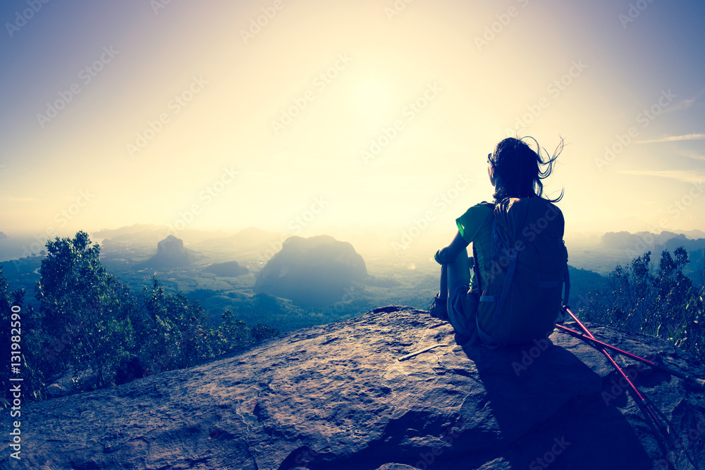 young traveler with backpack sit on the mountain peak rock observing locality