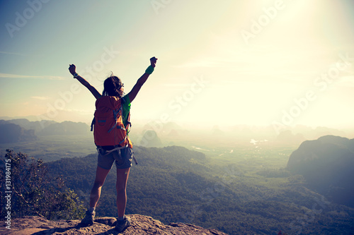 cheering young traveler with backpack on the mountain peak rock observing locality
