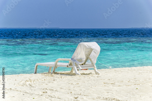 One white beach chair on the beach in front of turquoise water.