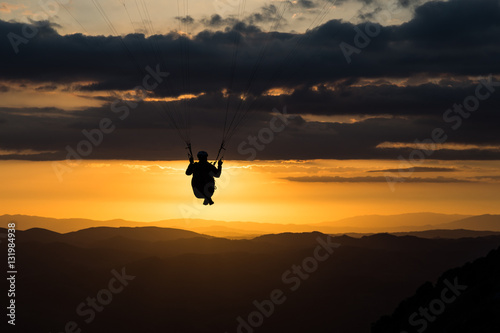 Beautiful shot of a paraglider silhouette flying toward the sunset, with beautiful orange colors and dark tones