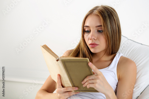 Young beautiful blonde woman lying in bed reading old book