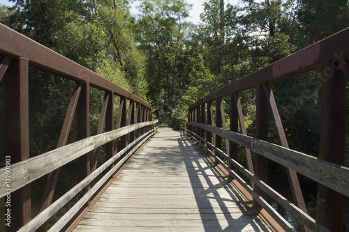 Wood and rusted metal bridge receding onto a wooded pathway