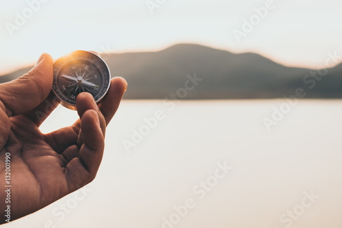 Fotografia Hand with compass at mountain road at sunset sky