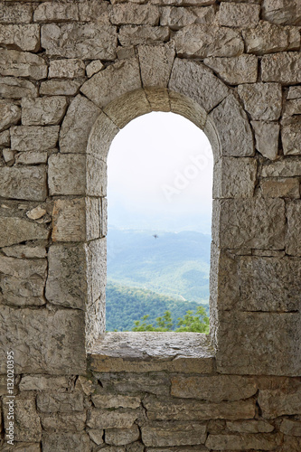 Stone war tower window with motional blurred bird and sea coast view with green tree hills