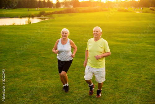 Elderly couple jogging. Smiling people on grass background. Former professional athletes. Health of cardiovascular system.