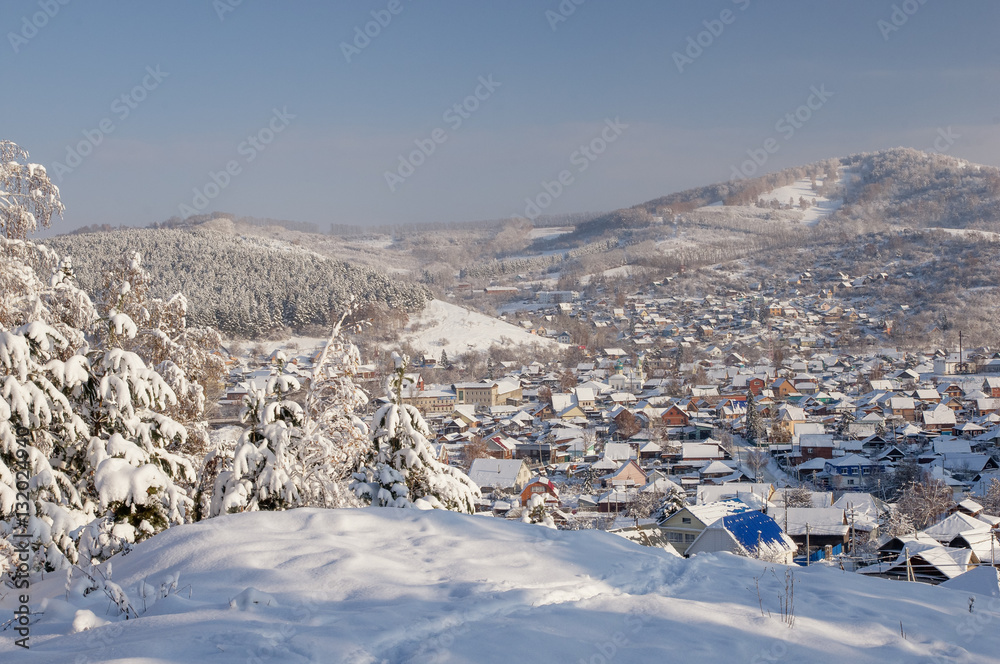 Winter snowy mountain valley with village town and slope with frozen rime pine trees in the foreground with ranges of snow hills on the background under blue sky Altai Mountains, Siberia, Russia