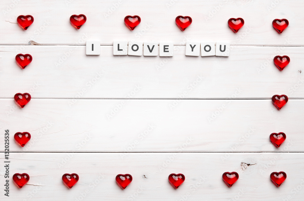 Texture of red heart figures shaped into frame with I love you phrase inside, on white wooden background Texture of red heart figures shaped into frame with I love you phrase inside, on white wooden background