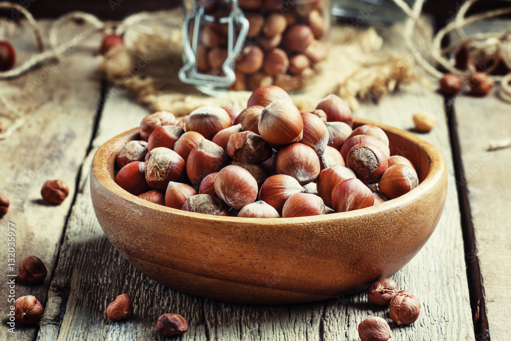 Raw hazelnuts in shell in a bowl on the old wooden background, s Raw hazelnuts in shell in a bowl on the old wooden background, s