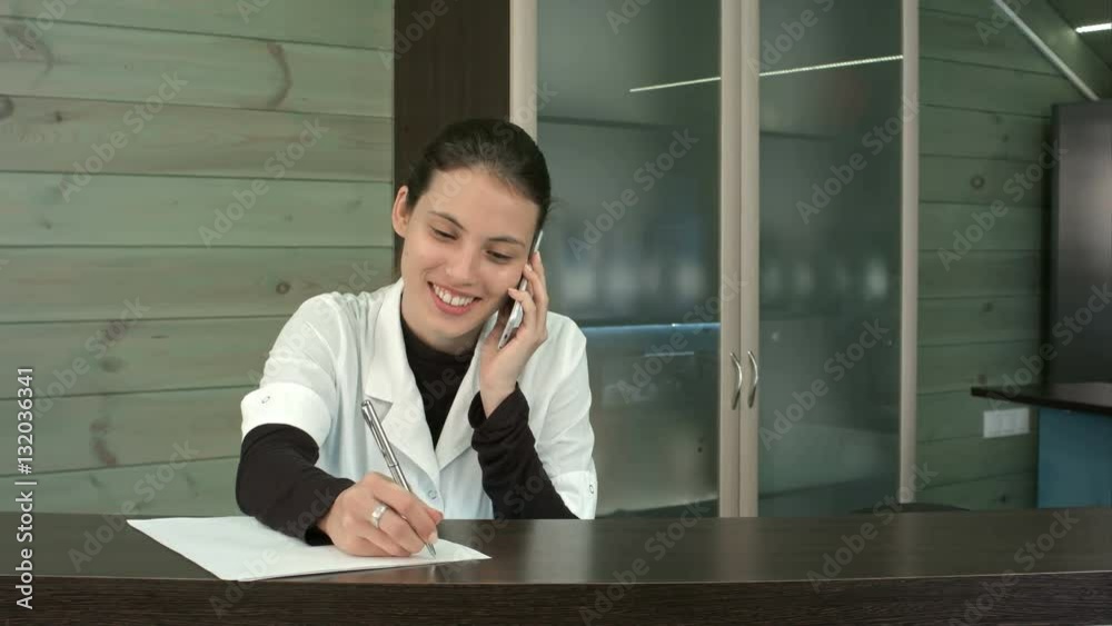 Smiling spa receptionist talking to client over the phone and filling in form Smiling spa receptionist talking to client over the phone and filling in form