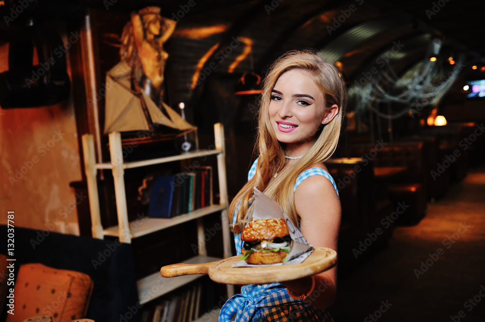 pretty girl waiter holding a delicious burger on a tray on a background of the restaurant pretty girl waiter holding a delicious burger on a tray on a background of the restaurant