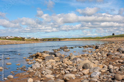 Small arched bridge over a river with rocky river bed running over the sandy beach into the Atlantic ocean at Lehinch in County Clare in Ireland 